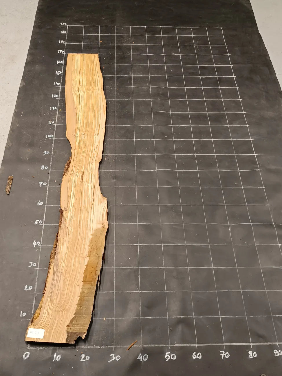 Planche bois d'olivier rabotée 2 cm à bord naturel, 180×28 cm, réf P29, sur tapis quadrillé 10 cm — recto