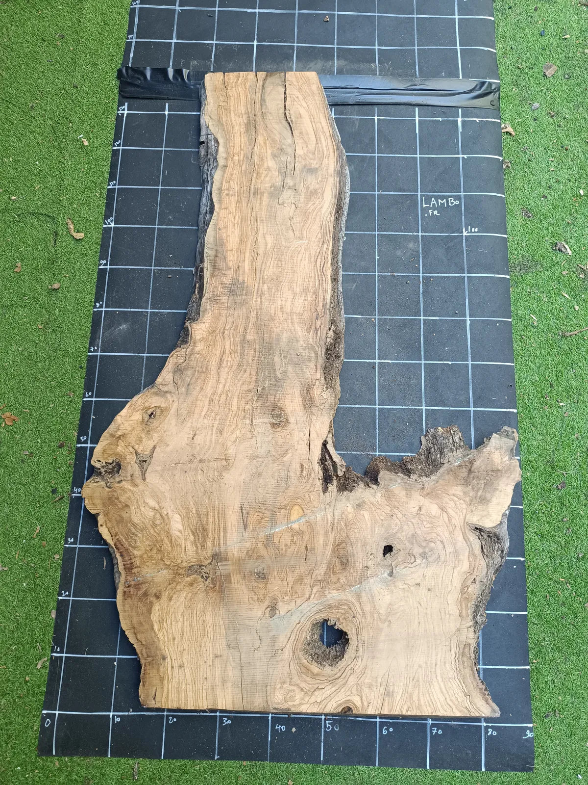 Plateau bois d'olivier brut à bord vivant 140×80 cm, réf N°008, sur tapis quadrillé 10 cm — recto