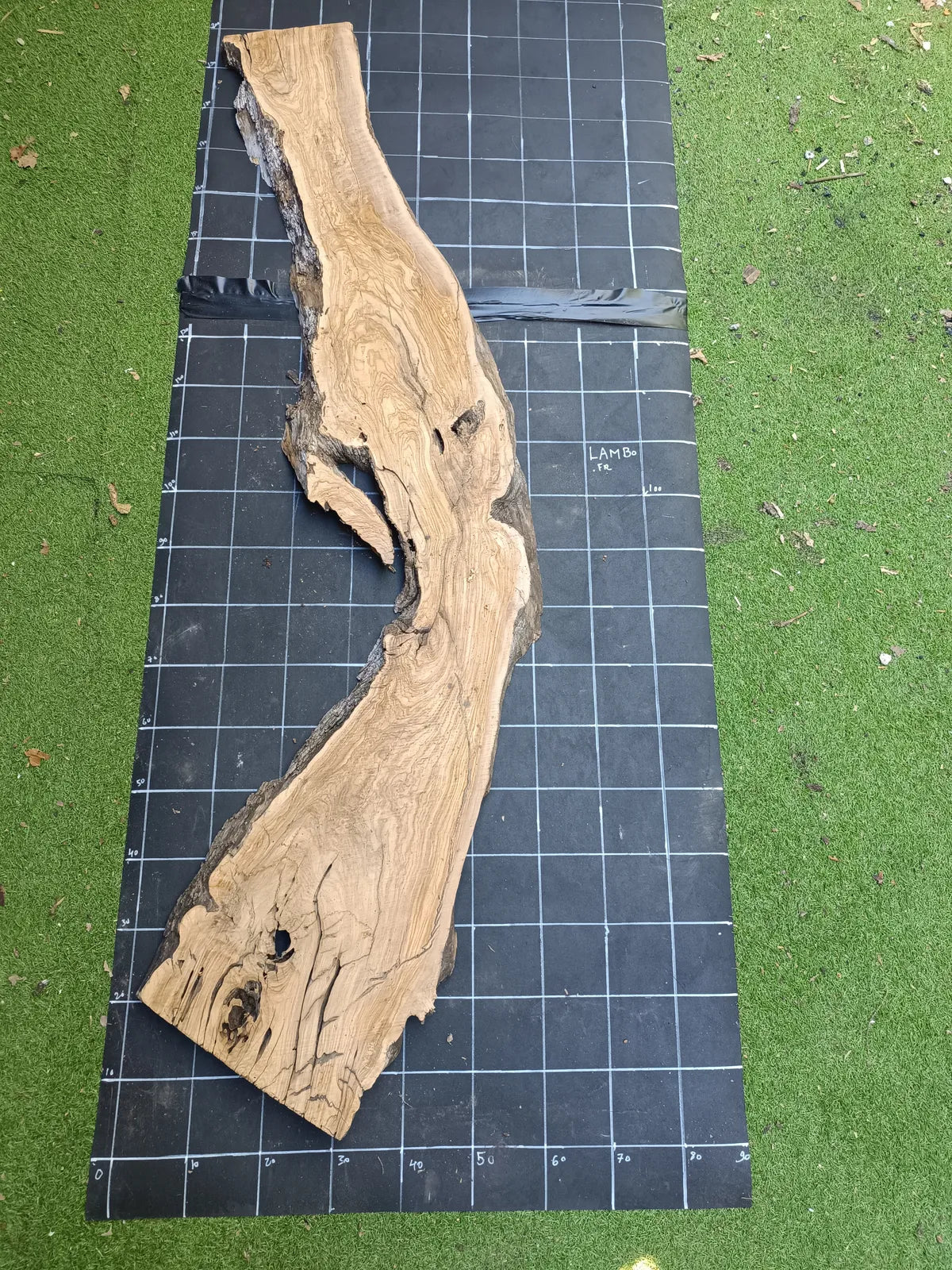 Plateau bois d'olivier brut à bord vivant 140×70 cm, réf N°012, sur tapis quadrillé 10 cm — recto