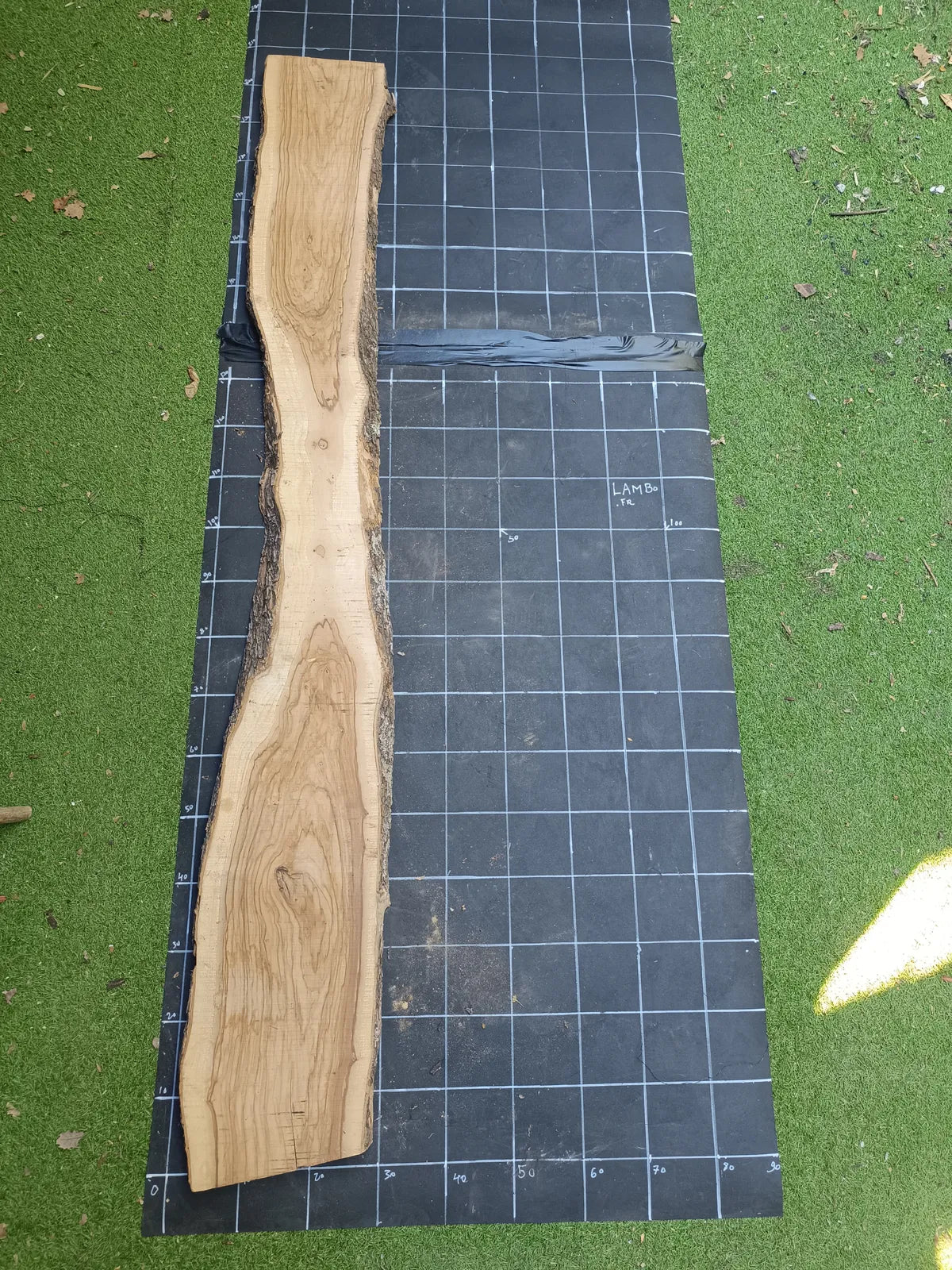 Plateau bois d'olivier brut à bord vivant 200×30 cm, réf N°027, sur tapis quadrillé 10 cm — recto