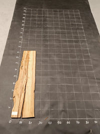 Planche bois d'olivier rabotée 2 cm à bord naturel, 140×30 cm, réf P34, sur tapis quadrillé 10 cm — recto