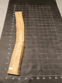 Planche bois d'olivier rabotée 2 cm à bord naturel, 175×25 cm, réf P21, sur tapis quadrillé 10 cm — verso