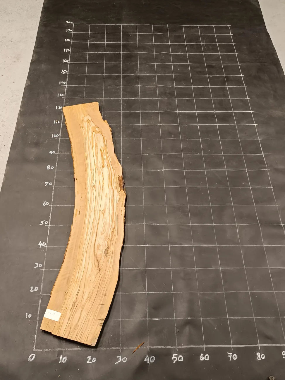 Planche bois d'olivier rabotée 2 cm à bord naturel, 175×28 cm, réf P19, sur tapis quadrillé 10 cm — recto