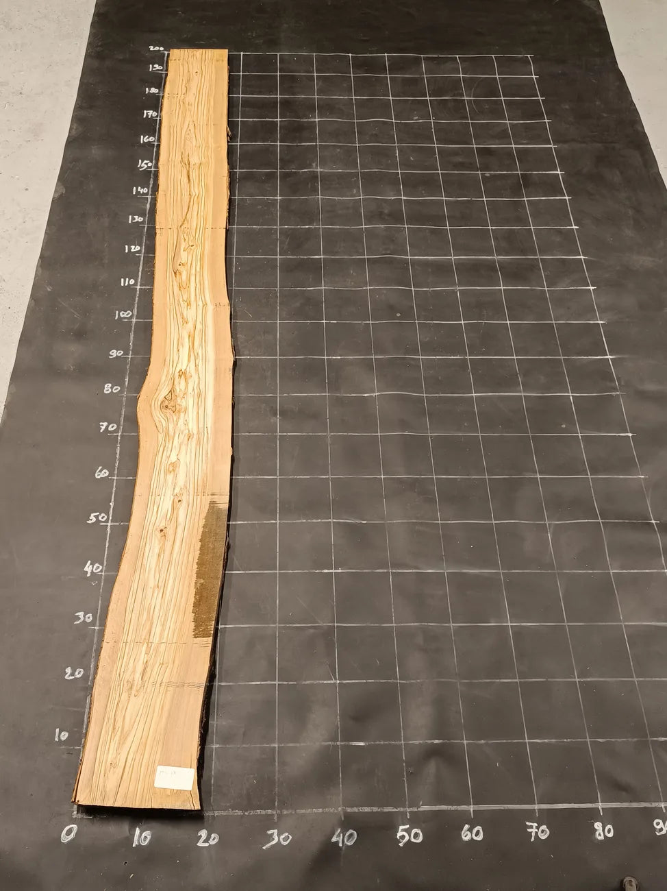 Planche bois d'olivier rabotée 2 cm à bord naturel, 180×25 cm, réf P17, sur tapis quadrillé 10 cm — recto