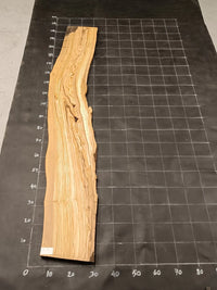 Planche bois d'olivier rabotée 2 cm à bord naturel, 180×28 cm, réf P18, sur tapis quadrillé 10 cm — recto