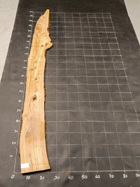 Planche bois d'olivier rabotée 2 cm à bord naturel, 180×28 cm, réf P25, sur tapis quadrillé 10 cm — verso