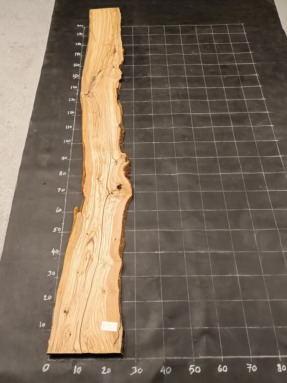 Planche bois d'olivier rabotée 2 cm à bord naturel, 185×28 cm, réf P07, sur tapis quadrillé 10 cm — recto