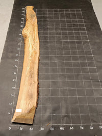 Planche bois d'olivier rabotée 2 cm à bord naturel, 185×28 cm, réf P22, sur tapis quadrillé 10 cm — verso