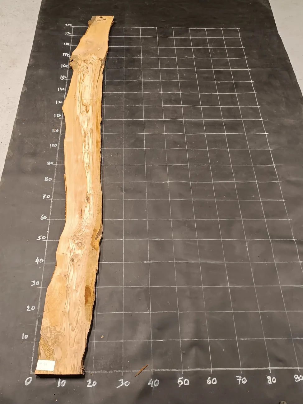 Planche bois d'olivier rabotée 2 cm à bord naturel, 185×28 cm, réf P24, sur tapis quadrillé 10 cm — recto