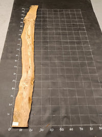 Planche bois d'olivier rabotée 2 cm à bord naturel, 185×28 cm, réf P24, sur tapis quadrillé 10 cm — recto