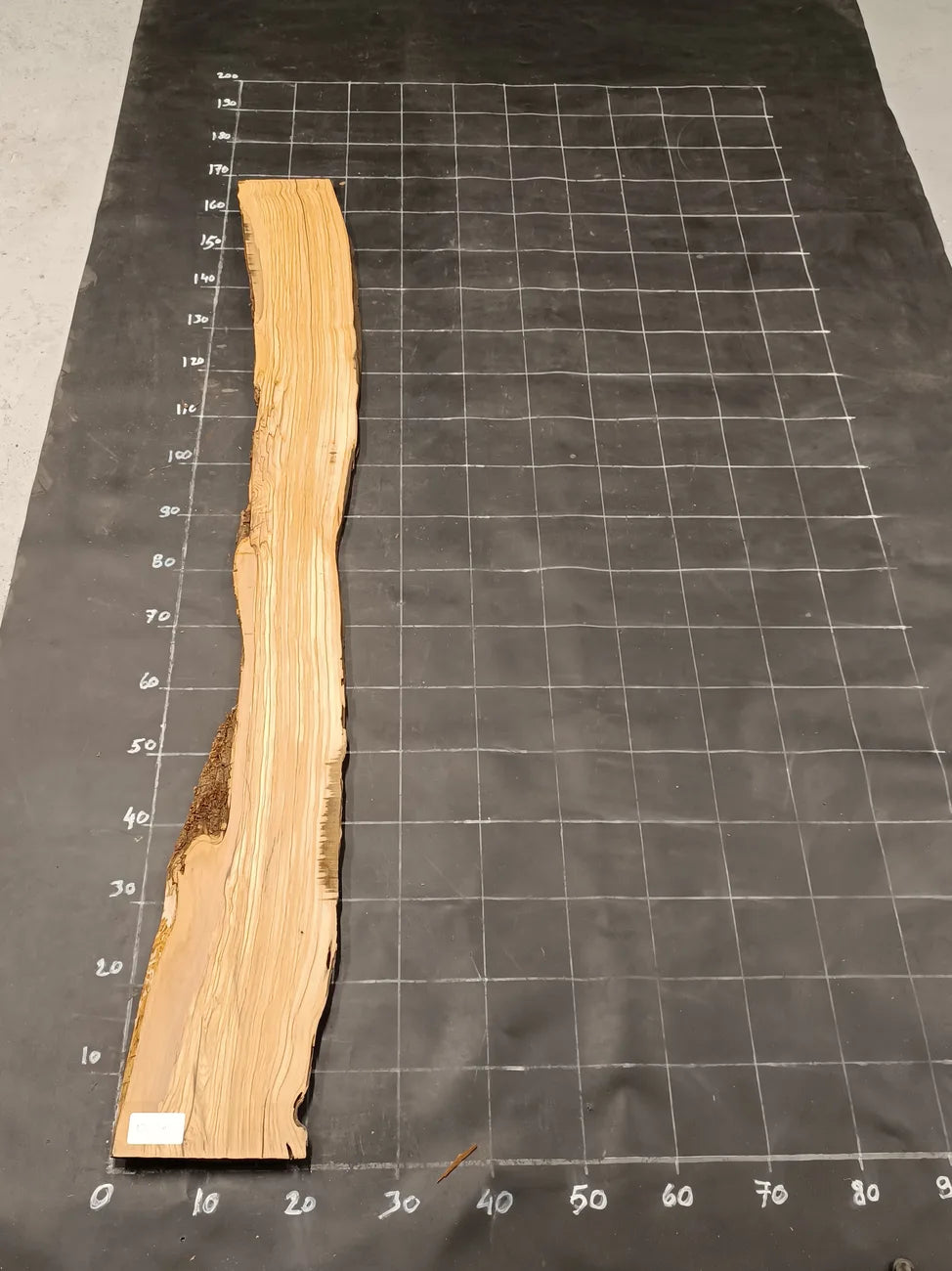 Planche bois d'olivier rabotée 2 cm à bord naturel, 185×30 cm, réf P20, sur tapis quadrillé 10 cm — recto