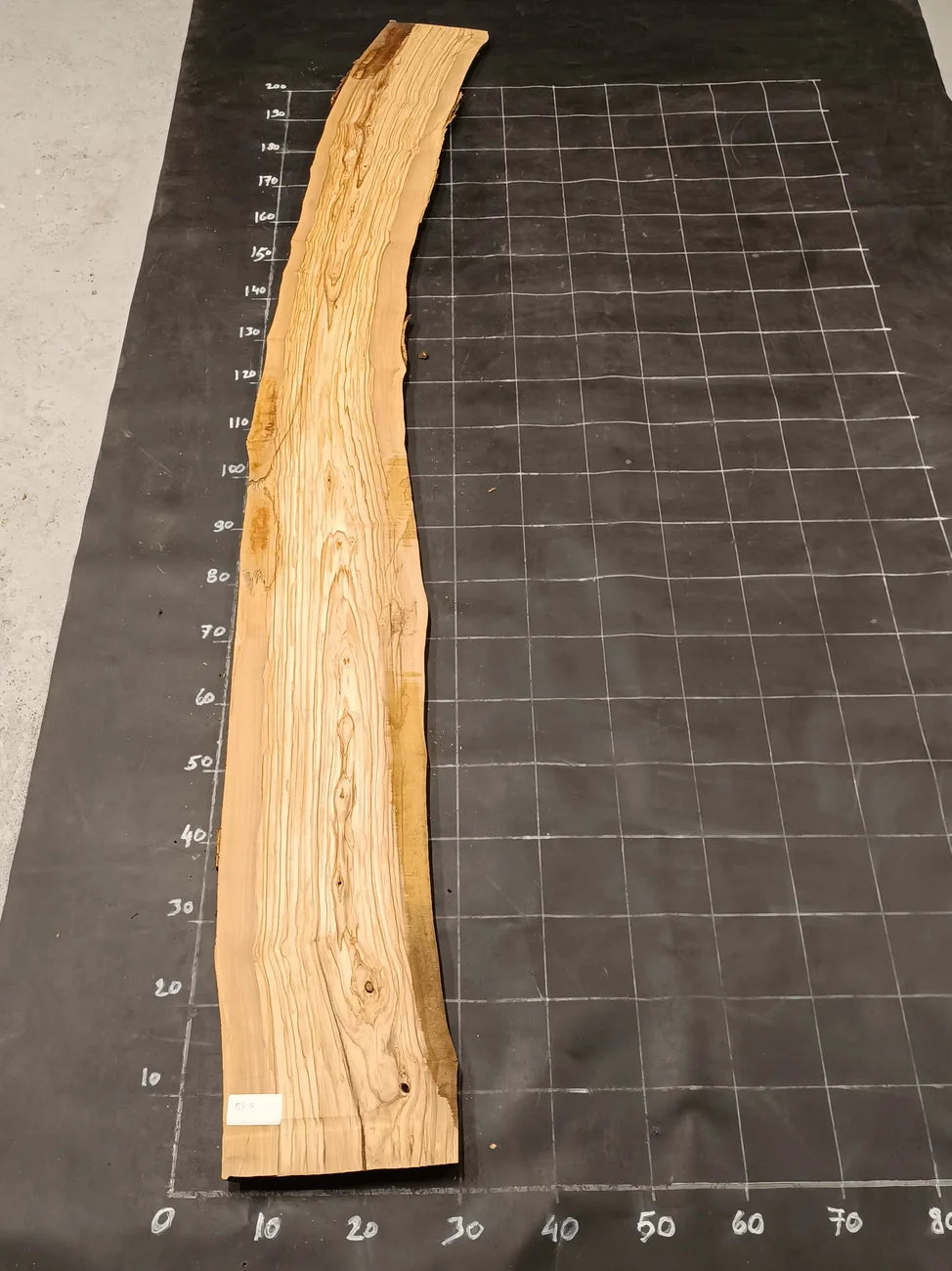 Planche bois d'olivier rabotée 2 cm à bord naturel, 190×28 cm, réf P05, sur tapis quadrillé 10 cm — recto