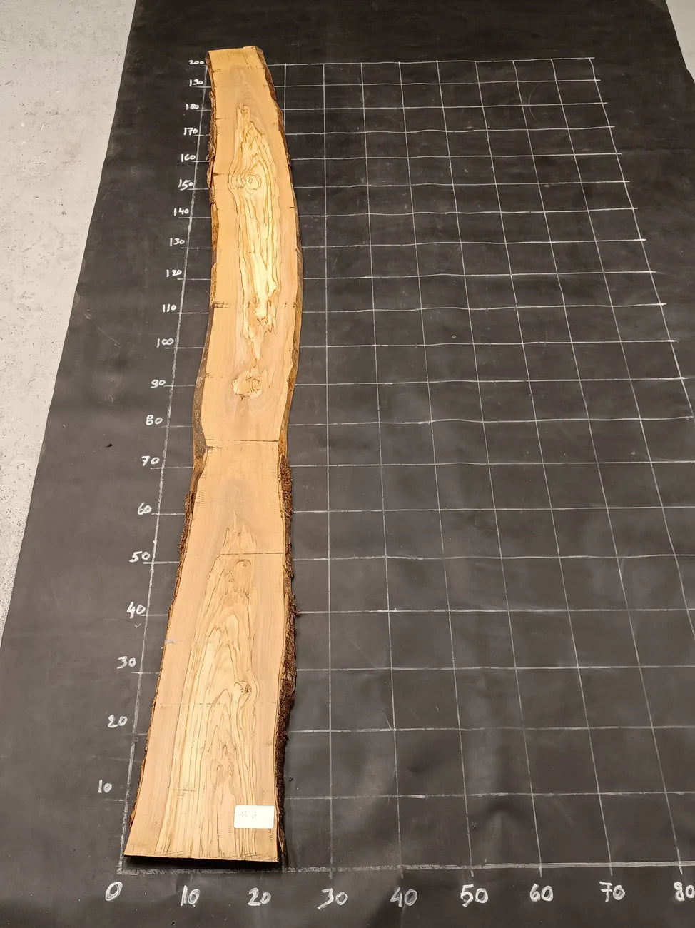 Planche bois d'olivier rabotée 2 cm à bord naturel, 190×30 cm, réf P06, sur tapis quadrillé 10 cm — recto