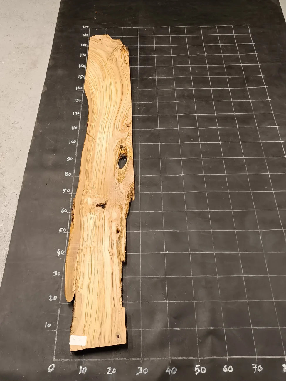 Planche bois d'olivier rabotée 2 cm à bord naturel, 190×32 cm, réf P12, sur tapis quadrillé 10 cm — recto